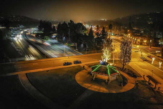 Aerial view of the 210 freeway with traffic light trails, featuring a decorated gazebo in a park during the Christmas season in Los Angeles County, California, United States.