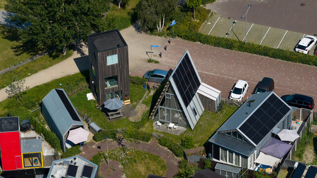 Aerial view of modern tiny houses and unique architectural cabins with solar panels, green gardens, and paved pathways in Almere, Flevoland, Netherlands.