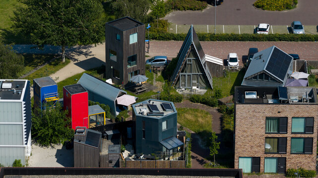 Aerial view of unique experimental houses with diverse architectural styles, including a tall wooden tower and an A-frame cabin, in Almere, Flevoland, Netherlands.