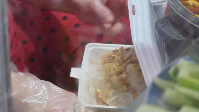Street food vendor preparing a take-away portion of traditional Vietnamese noodles in a styrofoam container