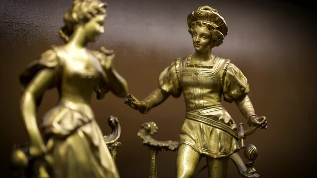 A golden bronze statue of a boy and girl figurine displayed as a decorative ornament photographed from a different angle on a dark background.