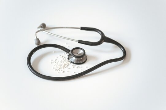 Black medical stethoscope over small white homeopathic pills on bright background evoking alternative medicine, holistic healthcare, and natural treatment marketing concepts.