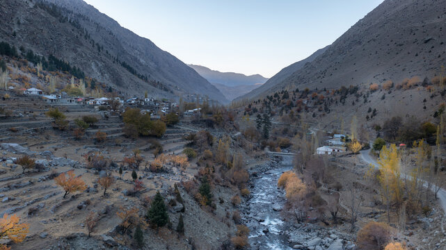 Aerial view of Astore Valley with a winding river, terraced fields, and a small village nestled among autumn-colored trees in the mountainous landscape of Astore, Gilgit, Pakistan.