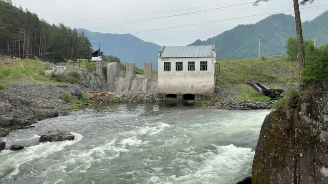 A wide shot shows the Chemal Hydroelectric Power Station with a turbulent river flowing past it in the Republic of Altai, Russia