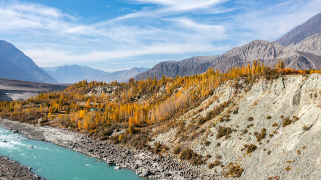 Aerial view of Nomal Valley featuring a turquoise river flowing through rocky terrain with vibrant autumn foliage on the slopes in Garelt, Gilgit, Pakistan.