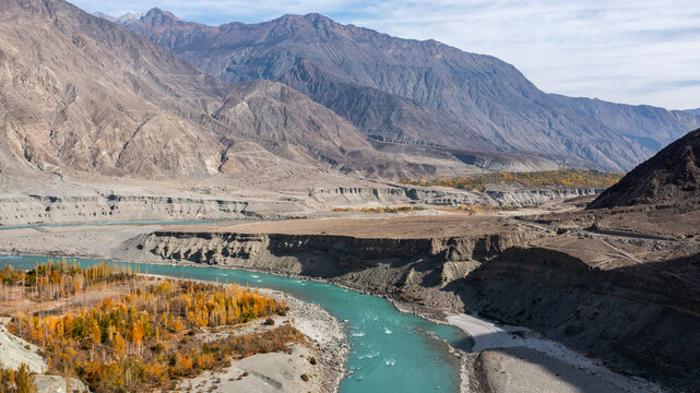 Aerial view of Nomal Valley featuring a turquoise river flowing through rugged mountain terrain with golden autumn trees and rocky slopes in Garelt, Gilgit, Pakistan.