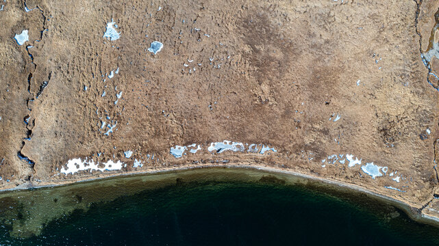 Aerial view of the shoreline of Sheosar Lake featuring patches of snow and dry alpine vegetation in Astore, Gilgit, Pakistan.