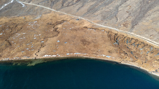 Aerial view of the serene Sheosar Lake surrounded by dry mountainous terrain, patches of snow, and a winding dirt road in Astore, Gilgit, Pakistan.