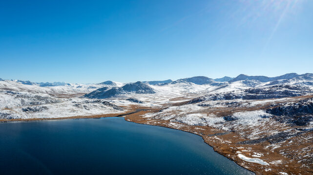 Aerial view of Sheosar Lake surrounded by snow-capped mountains and golden-brown alpine meadows under a clear blue sky in Astore, Gilgit, Pakistan.