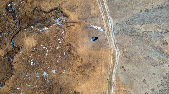 Aerial view of a vehicle parked on a dirt road in the vast, arid, and partially snow-dusted high-altitude plateau of Deosai National Park, Astore, Gilgit, Pakistan.
