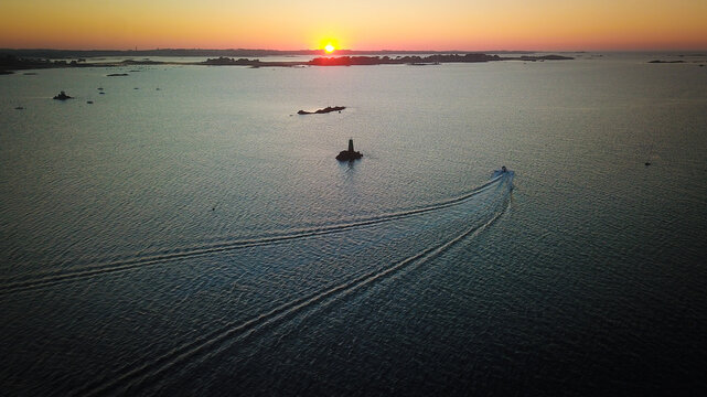 Aerial view of the Louet island lighthouse at sunset with a boat leaving a wake in the calm sea in Carantec, Brittany, France.