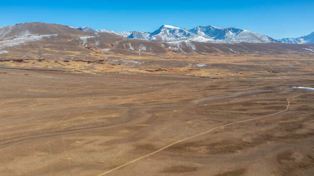 Aerial view of Deosai National Park featuring vast high-altitude plains, snow-capped mountain peaks, and winding dirt tracks in Astore, Gilgit, Pakistan.