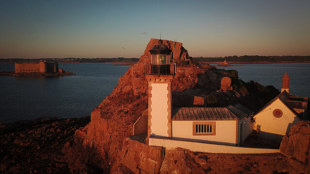 Aerial view of the lighthouse on Louet island at sunset with Chateau du Taureau in the background, surrounded by the calm waters of the bay in Carantec, Brittany, France.