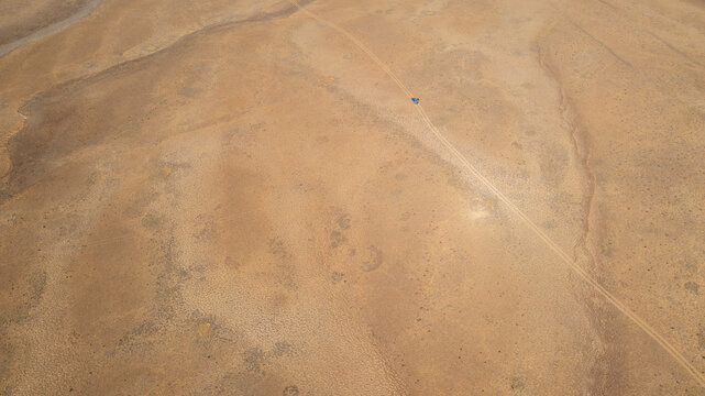 Aerial view of the vast, arid landscape of Deosai National Park with a dirt track winding through the terrain and a small vehicle in Astore, Gilgit, Pakistan.