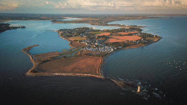 Aerial view of Tour des Anglais lighthouse situated on the coast of the Kervoyal peninsula with agricultural fields, coastal village, and calm blue waters in Damgan, Brittany, France.