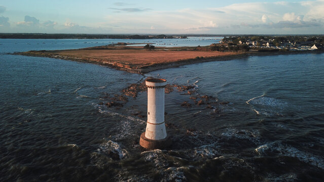 Aerial view of the Tour des Anglais lighthouse standing in the sea off the coast with rocky outcrops and a grassy peninsula in the background in Damgan, Brittany, France.