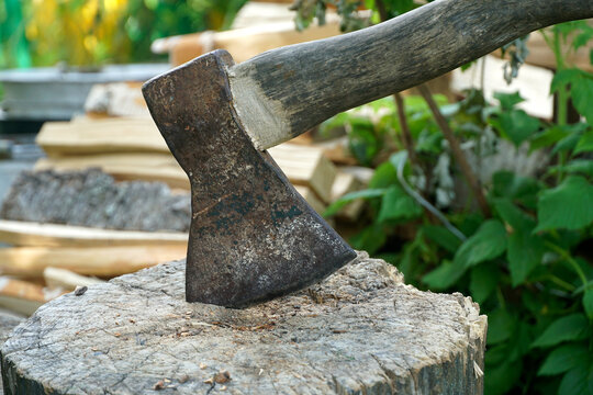 An old axe stuck into a block of wood against a background of chopped firewood. A village farm.