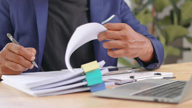 Business professional reviewing documents and financial reports at office desk with laptop and organized paperwork. Concept of document management, compliance audit, administration, contract review