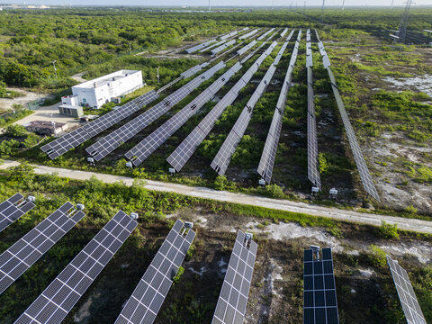 Aerial view of San Ignacio solar photovoltaic power plant with rows of solar panels, white maintenance building, and surrounding vegetation in Progreso, Yucatan, Mexico.