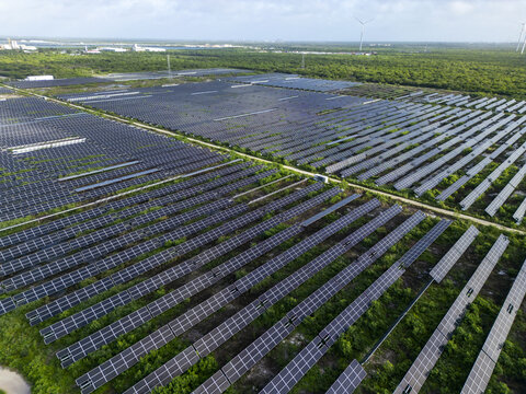 Aerial view of San Ignacio solar photovoltaic power plant featuring rows of solar panels in a rural landscape with green vegetation and distant wind turbines in Progreso, Yucatan, Mexico.