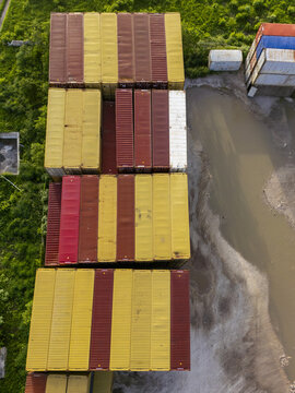 Aerial view of colorful shipping containers stacked in rows at the port of Puerto Progreso, with muddy ground and green vegetation nearby in Progreso, Yucatan, Mexico.