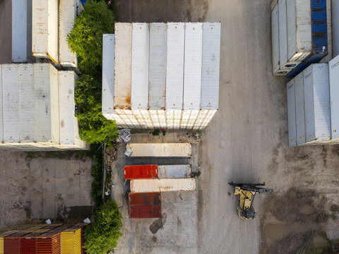 Aerial view of Puerto Progreso shipping container yard with stacked white containers, a yellow reach stacker vehicle, and surrounding greenery in Progreso, Yucatan, Mexico.