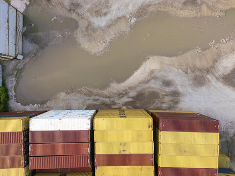 Aerial view of stacked colorful shipping containers at Puerto Progreso, with muddy ground and puddles nearby in Progreso, Yucatan, Mexico.