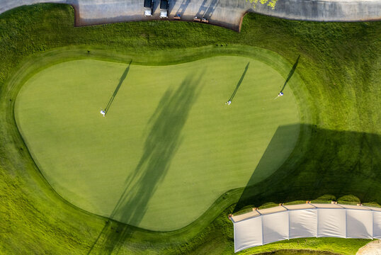 Aerial view of Provincia Golf Club with golfers on the putting green, long shadows, golf carts, and a white canopy structure in Merida, Yucatan, Mexico.