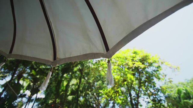 White beach umbrella beneath tropical green trees