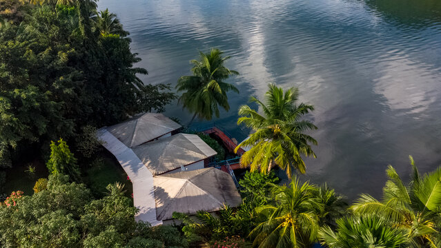 Aerial view of a waterfront resort with white-roofed buildings nestled among lush palm trees and dense tropical vegetation along the Volta River in Atimpoku, Volta Region, Ghana.