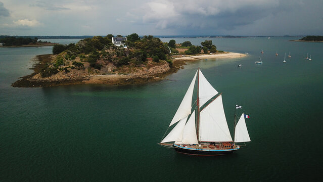 Aerial view of a traditional sailboat sailing near the Golf du Morbihan with lush island greenery and calm waters in Sarzeau, Brittany, France.
