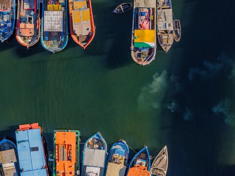 Aerial view of colorful fishing boats moored at Quadrado da Urca in the harbor, with calm green water and shadows cast on the surface in Rio de Janeiro, Rio de Janeiro, Brazil.