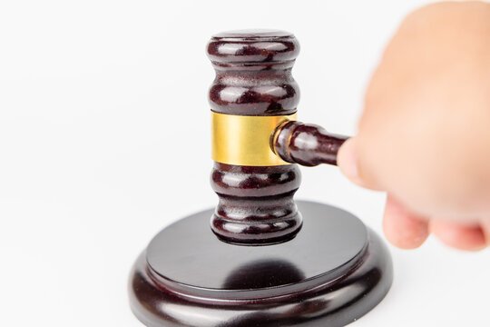 Front angle layout of a person hand striking a mahogany judge gavel down on its wooden sound block over a seamless white background