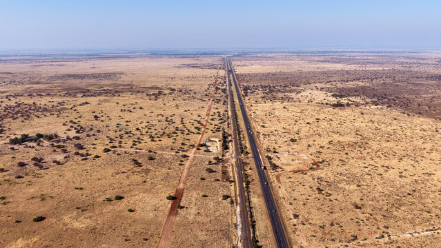 Aerial view of the Karoo landscape featuring a long straight highway and railway line cutting through the arid, dry shrubland in Beaufort West, Western Cape, South Africa.