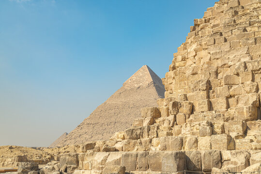 The three pyramids of the Giza plateau, Cairo, Egypt. A corner of the Cheops pyramid in the foreground. Khafre pyramid in the middle, Menkaure pyramid on the background, with blue sky.