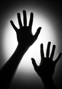 Silhouette of Human Hands Reaching Out Against a Bright Light Backgrou
