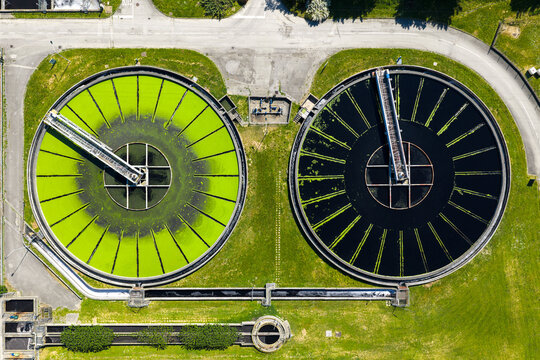 Aerial view of circular wastewater treatment tanks with green and dark water, surrounded by grass and paved paths in Prato, Tuscany, Italy.