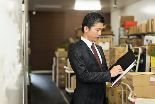 冷蔵庫前でクリップボードを確認する40代男性店長