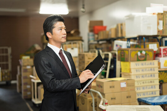 冷蔵庫前でクリップボードを確認する40代男性店長