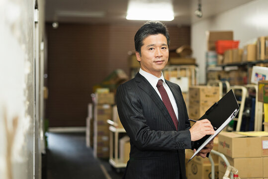 冷蔵庫前でクリップボードを確認する40代男性店長