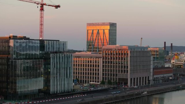 The setting sun reflects off glass buildings along Dublin's waterfront, highlighting the city's modern architectural style. Ideal for urban development features or travel content.