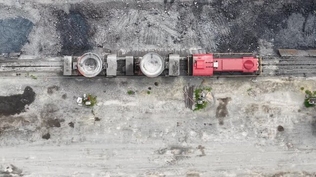 An industrial railway line with a red locomotive and specialized wagons observed from directly above.