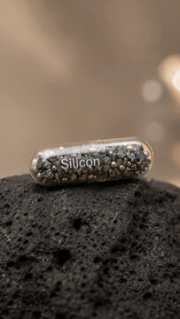 Small capsule containing silicon stands on a piece of black volcanic rock under soft light in a studio setting