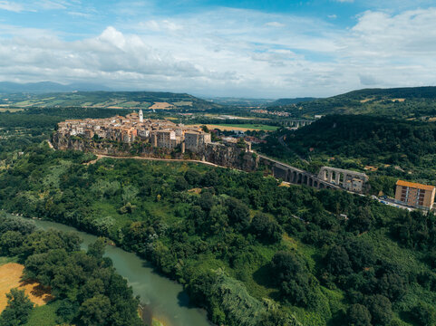 Aerial view of the historic town of Orte perched on a tuff cliff overlooking the Tiber river valley surrounded by lush green hills under a cloudy sky in Orte, Lazio, Italy.