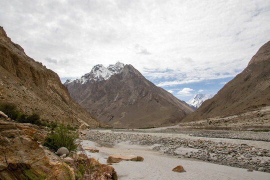 View of K2 Base Camp surrounded by rugged mountain peaks, a rocky riverbed, and a cloudy sky in Ghakhar, Gilgit, Pakistan.