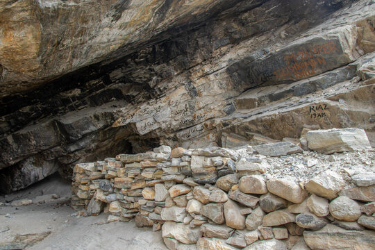 View of a rock shelter with a dry-stone wall and inscriptions on the rock face at K2 Base Camp in Ghakhar, Gilgit, Pakistan.