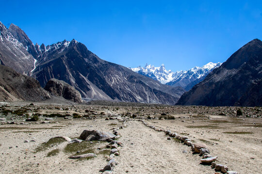 View of K2 Base Camp with rocky terrain and snow-capped mountains under a clear blue sky in Ghakhar, Gilgit, Pakistan.