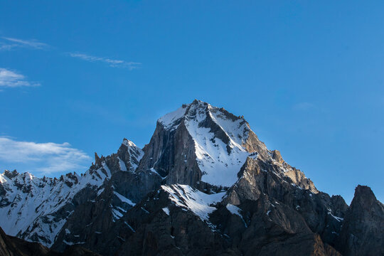View of K2 peak with snow-covered slopes and rocky ridges under a clear blue sky in Gilgit, Pakistan.