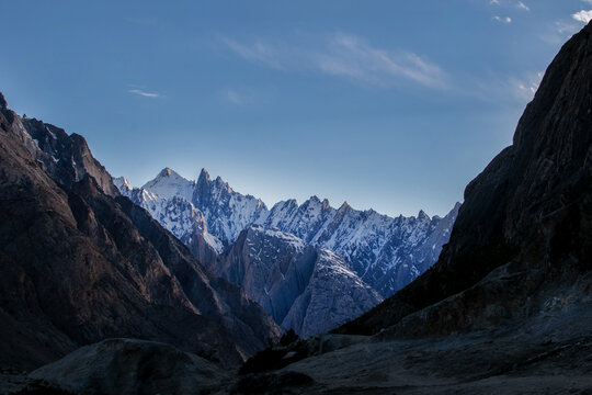 View of the majestic snow-capped peaks of the Karakoram range near K2 Base Camp, featuring rugged rocky slopes and deep shadows under a clear blue sky in Ghakhar, Gilgit, Pakistan.