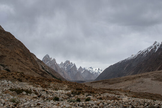 View of K2 Base Camp featuring rugged rocky terrain and towering snow-capped peaks under a dramatic cloudy sky in the Karakoram mountain range, Gilgit, Pakistan.